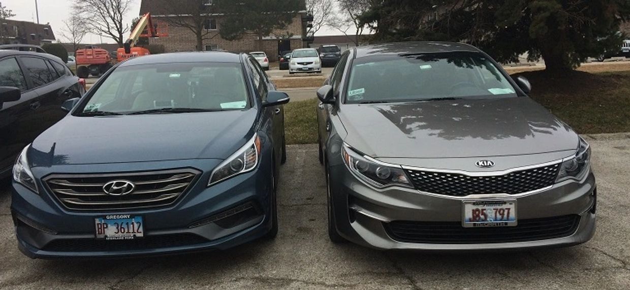 Two parked sedans, a blue Hyundai and a gray Kia, side by side in a parking lot.